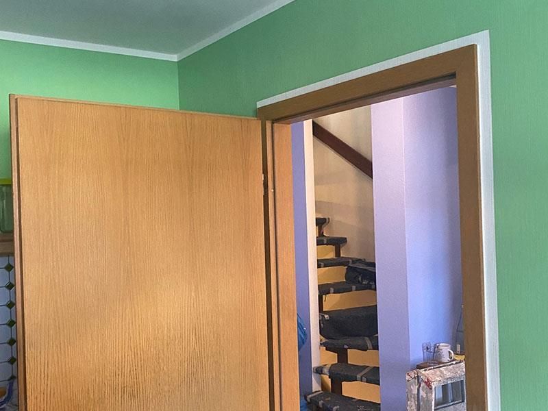 In einem Raum führt eine Holztür zu einer Treppe hin offen.