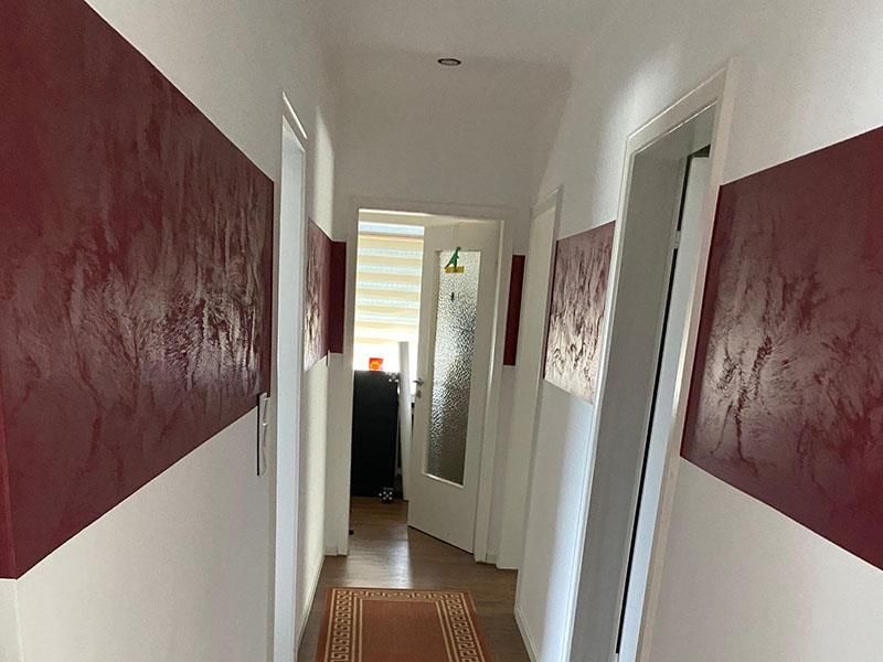 Ein Flur mit roten und weißen Wänden und einer Tür, die zu einem Zimmer führt.