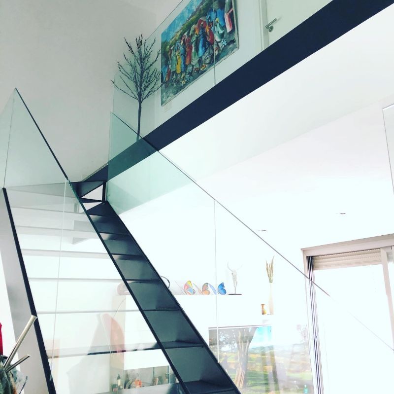 Una escalera con barandilla de cristal y una pintura en la pared encima.