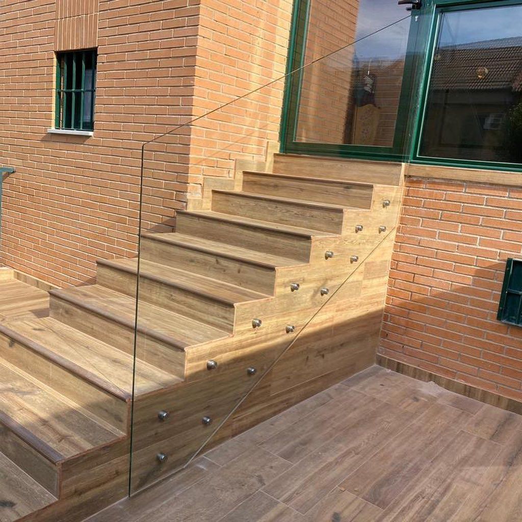 Un conjunto de escaleras de madera con barandilla de vidrio frente a un edificio de ladrillo.