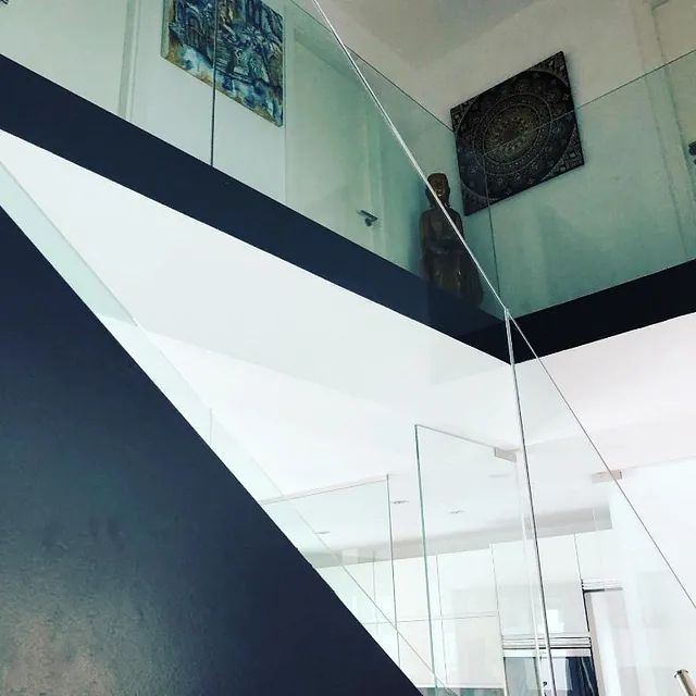 Una escalera con barandilla de cristal y un cuadro en la pared.