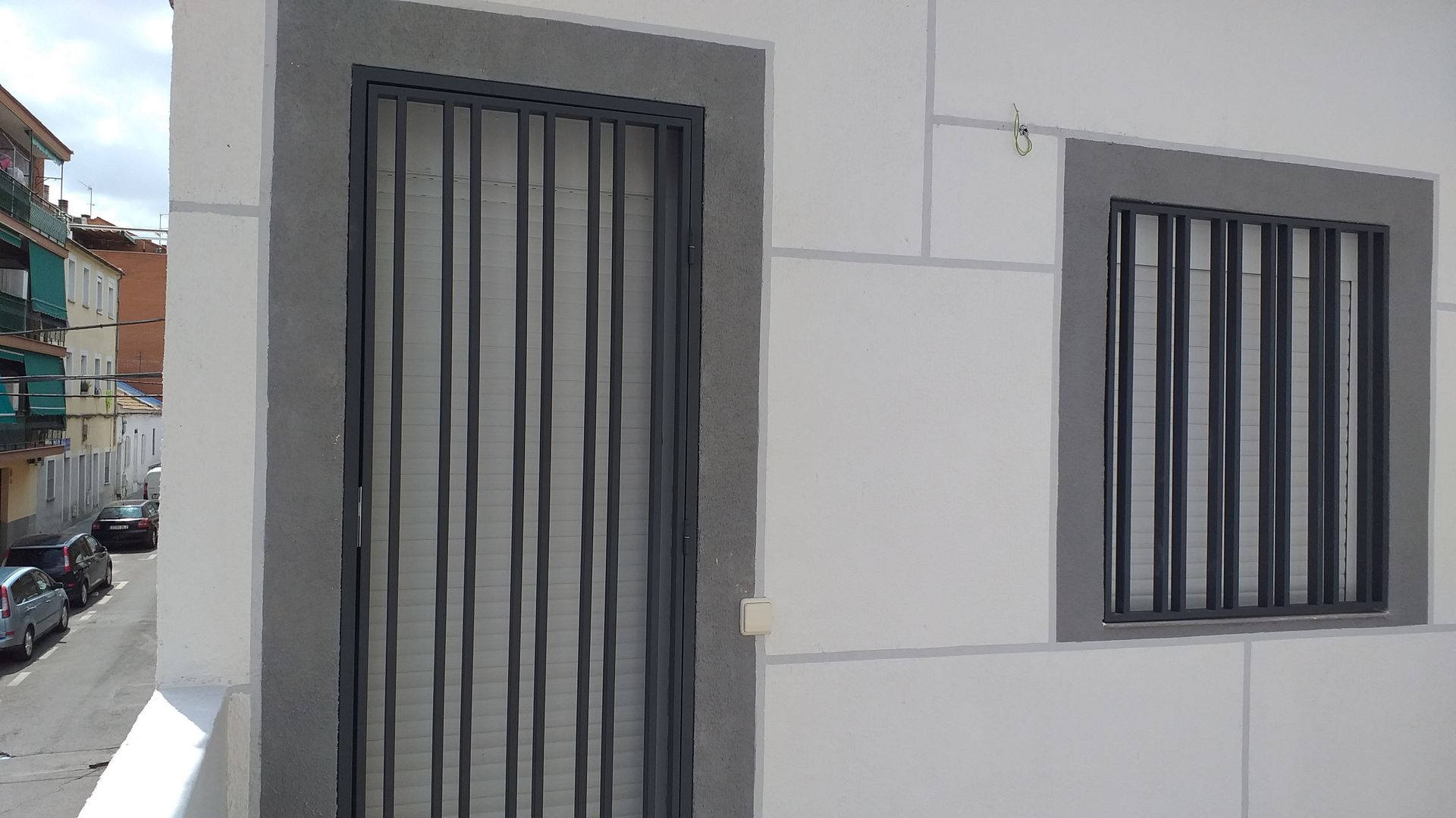 Un edificio blanco con una puerta de hierro forjado y dos ventanas.