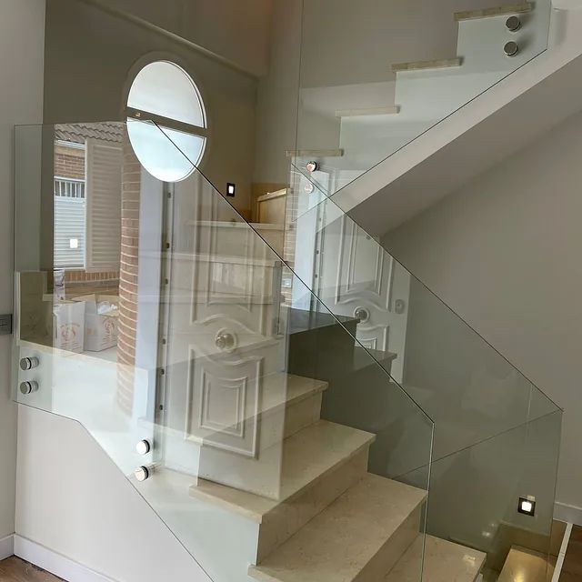 Una escalera con barandilla de cristal y una ventana redonda.