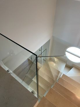 Una escalera con barandilla de cristal y escalones de madera en una casa.