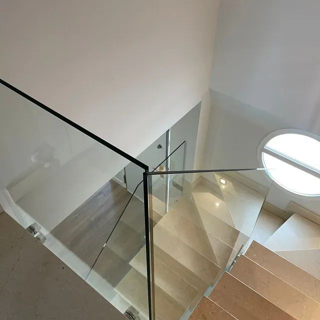 Una escalera con barandilla de cristal y una ventana redonda.