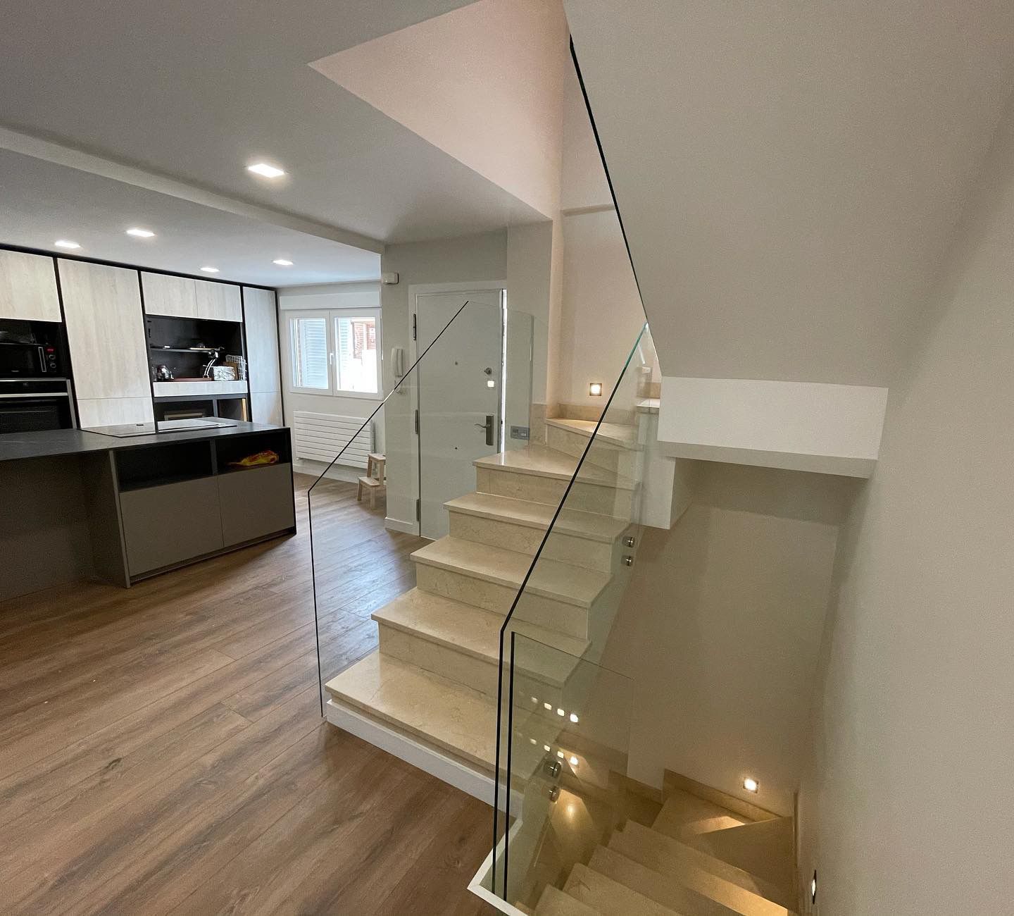 Una escalera con barandilla de vidrio que conduce al segundo piso de una casa.