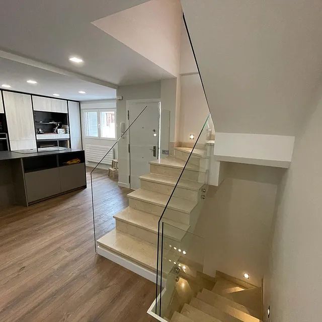 Una escalera con barandilla de vidrio que conduce al segundo piso de una casa.