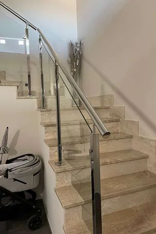 Una escalera con barandilla de cristal y un cochecito al lado.