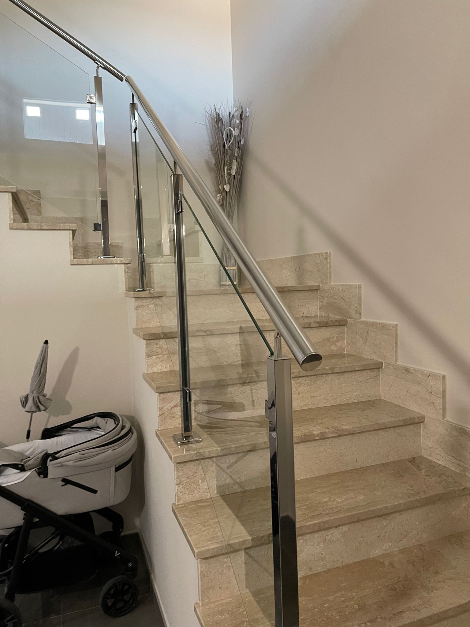 Una escalera con barandilla de cristal y un cochecito en la esquina.