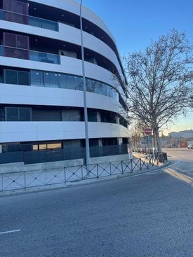 Un gran edificio está situado en la esquina de una calle al lado de un árbol.