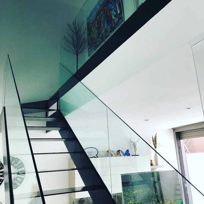 Una escalera con barandilla de cristal y un reloj en la pared.