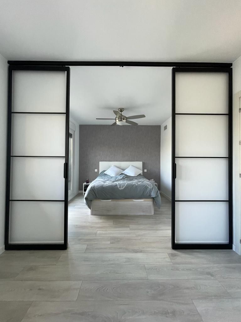 Un dormitorio con puertas corredizas de vidrio que conducen a una cama y un ventilador de techo.