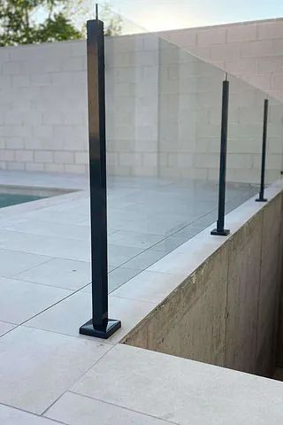 Un primer plano de una barandilla de vidrio junto a una piscina.