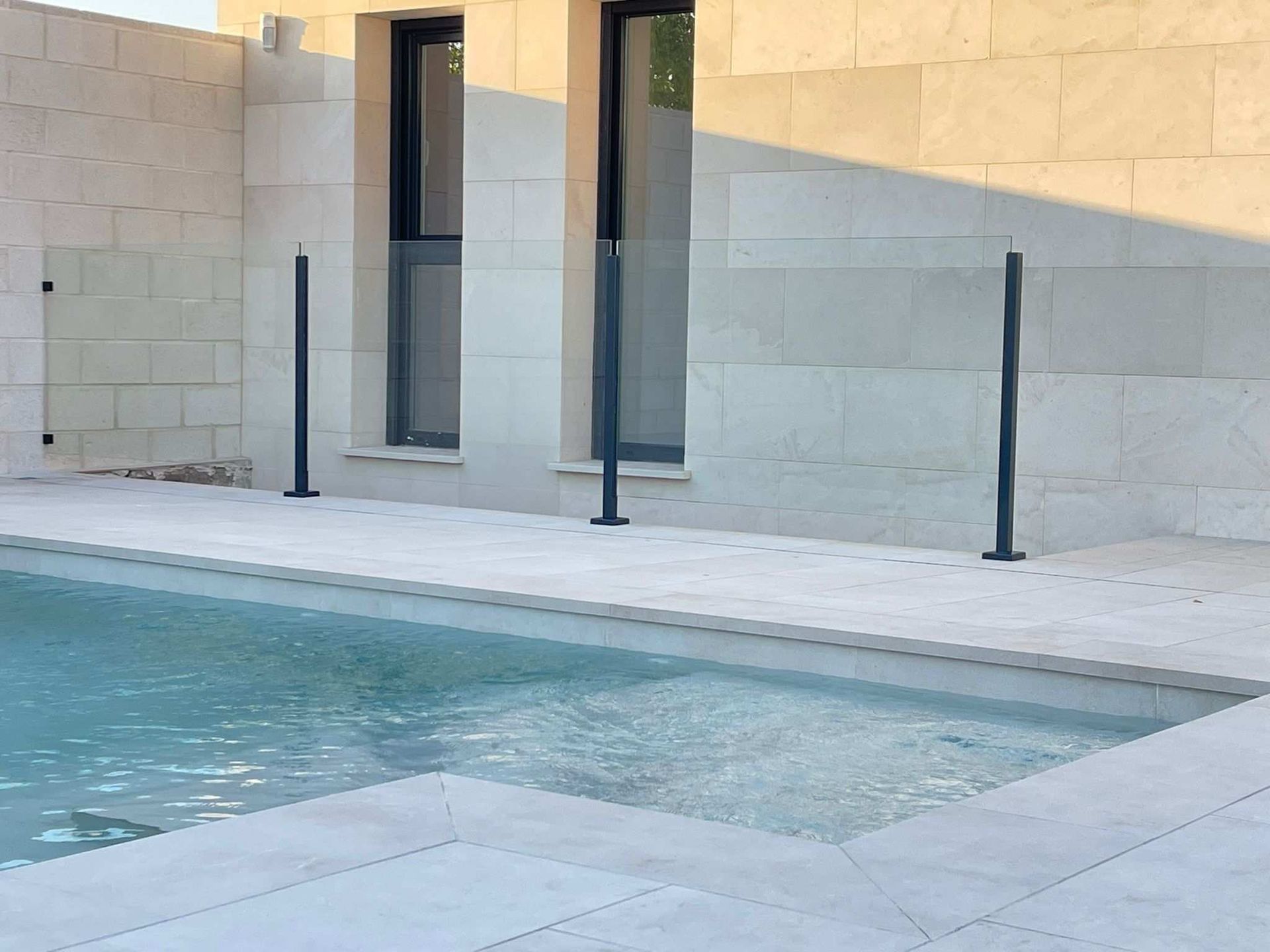 Una piscina está rodeada por un muro de piedra y una valla de cristal.