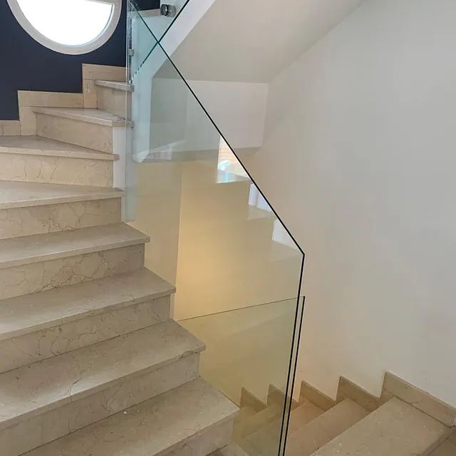 Una escalera con barandilla de cristal y una ventana redonda.