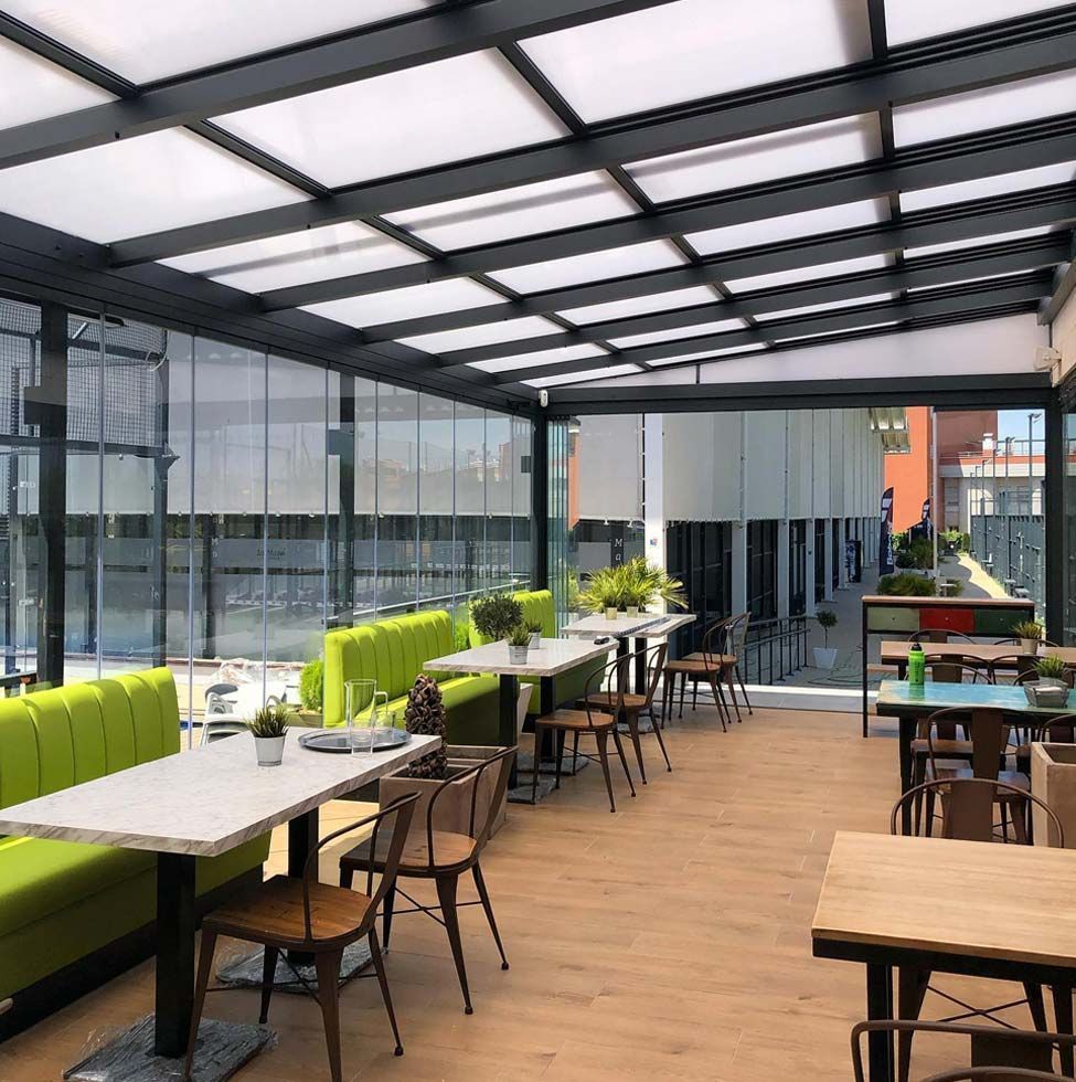 Un restaurante con mesas y sillas bajo un techo de cristal.