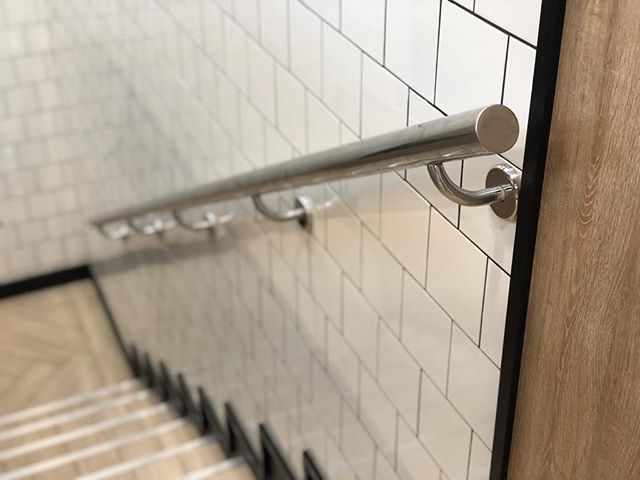 Una escalera con pasamanos de acero inoxidable contra una pared de azulejos blancos.