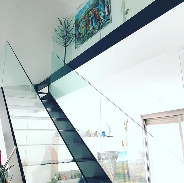 Una escalera con barandilla de cristal y una pintura en la pared encima.