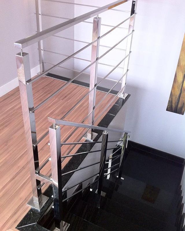 Una escalera con barandilla de acero inoxidable y escalones negros.