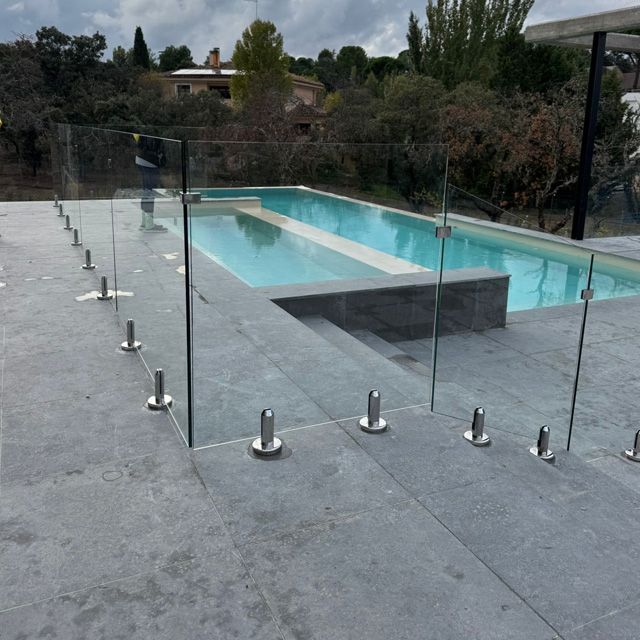 Cerca de vidrio para piscina con postes de acero inoxidable alrededor de una piscina rectangular en un patio.