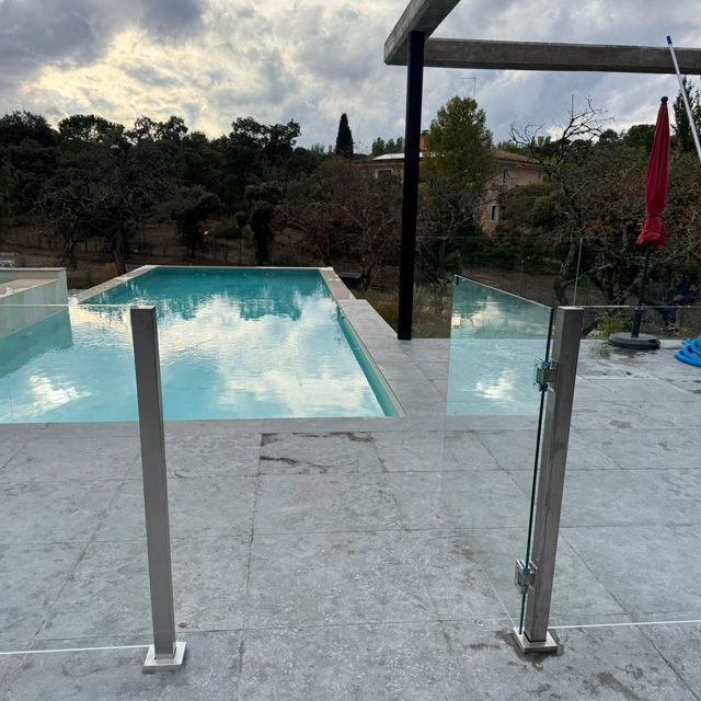 Piscina con barandilla de cristal y cielo nublado.