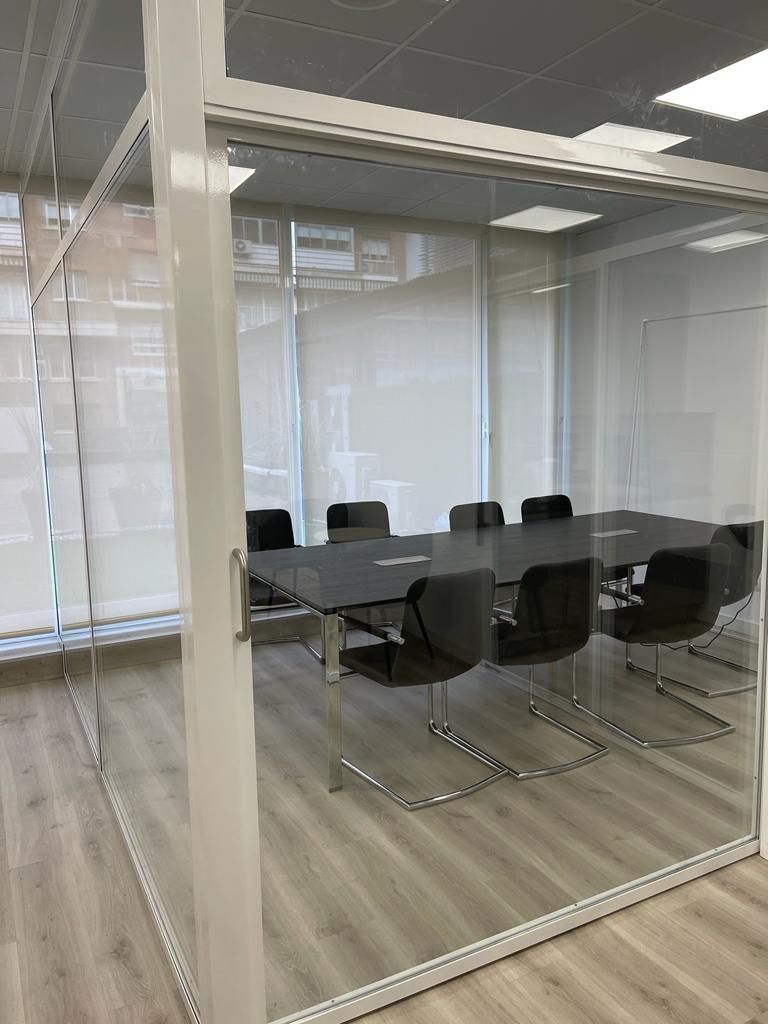 Una sala de conferencias con una pared de cristal y una mesa y sillas.