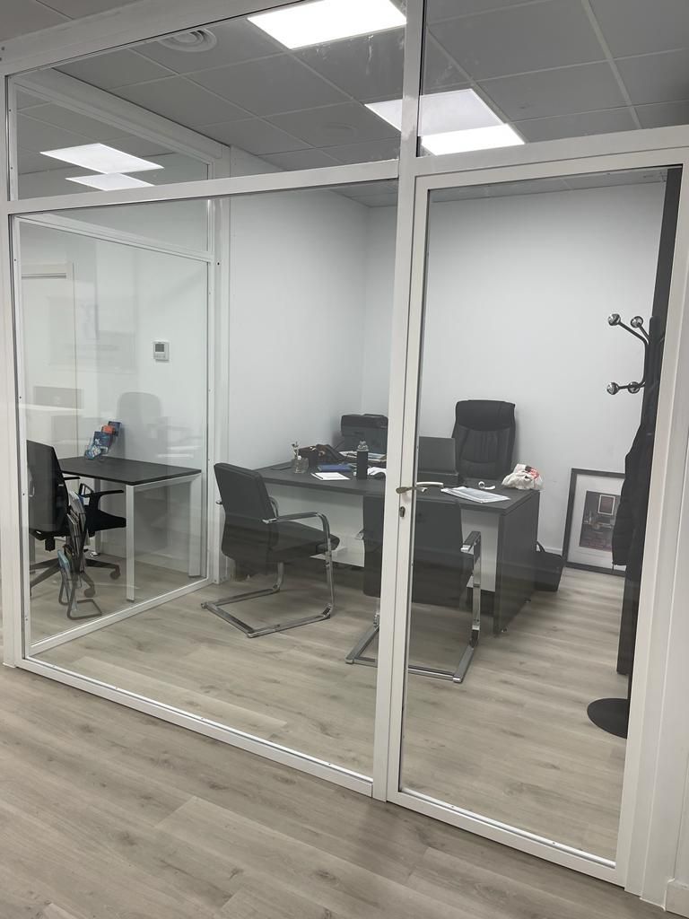 Una habitación con un escritorio y sillas con una pared de vidrio.