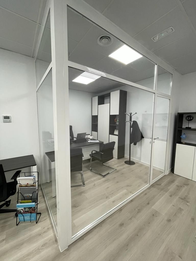 Una pequeña oficina con una pared de cristal y un escritorio y sillas.