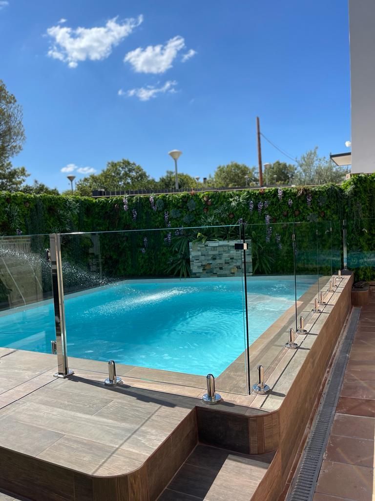 Una gran piscina con una valla de cristal y una cascada al fondo.