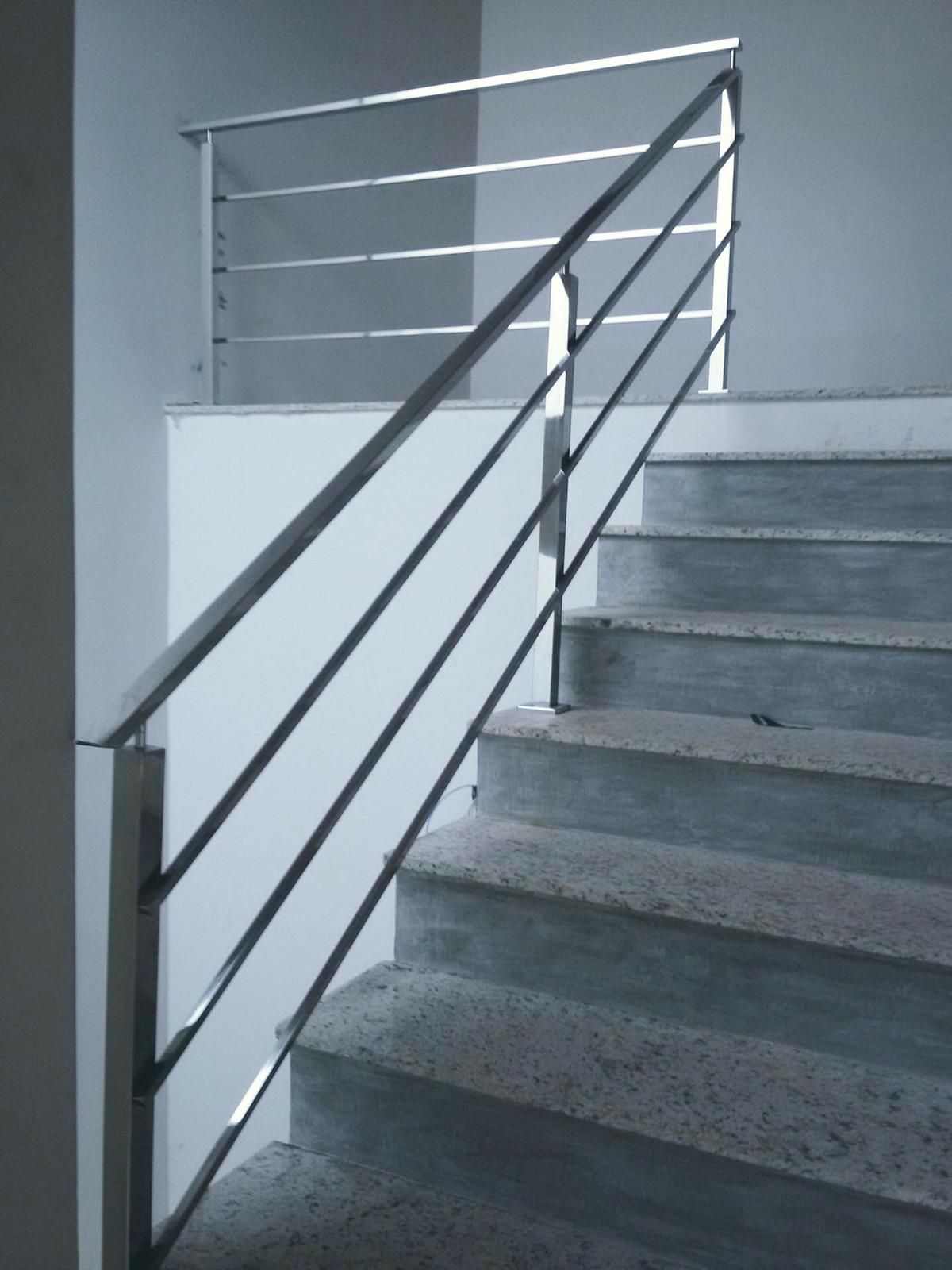 Una escalera con barandilla de metal y una pared blanca.