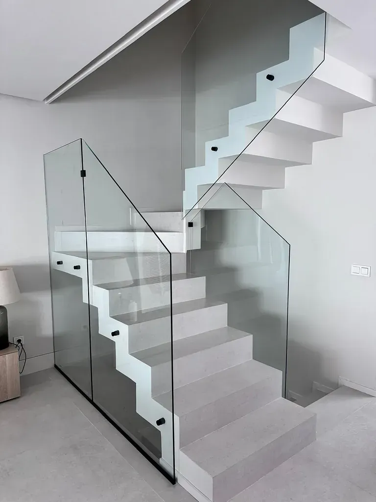 Una escalera blanca con barandilla de cristal en una habitación.