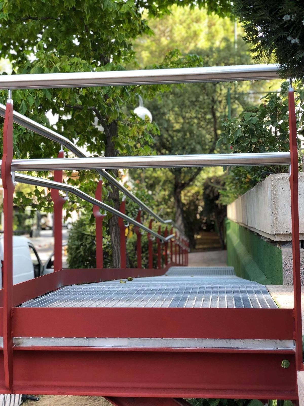 Una escalera roja con barandilla de metal que conduce a un camino.