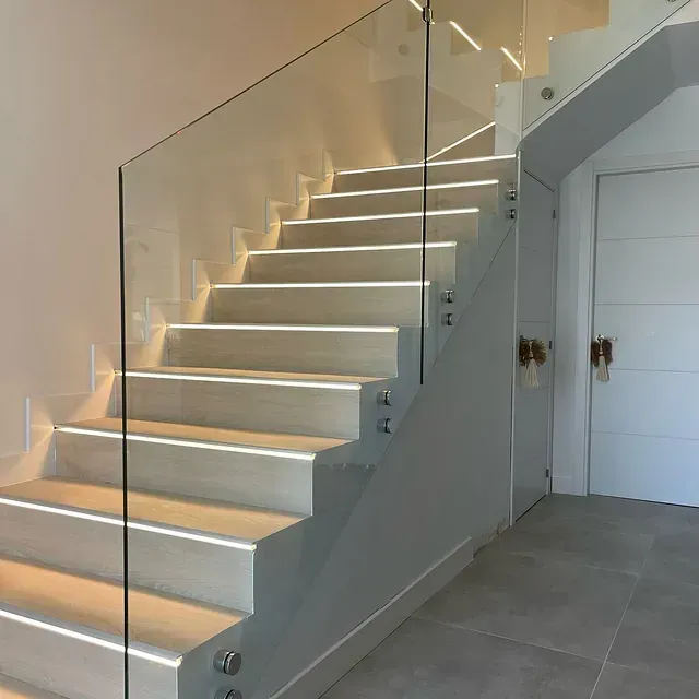 Una escalera con barandilla de cristal en un pasillo.