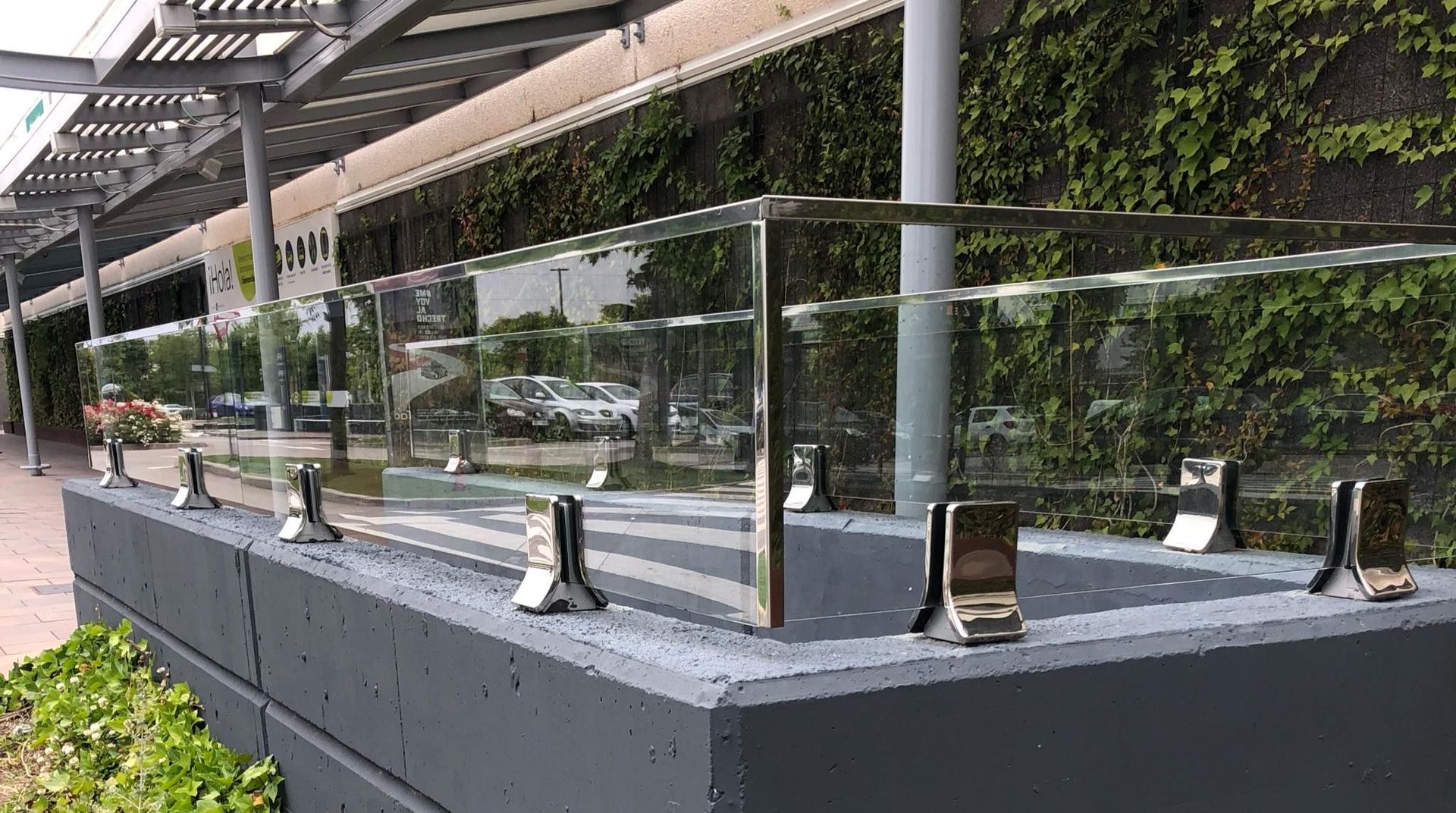 Una valla de vidrio está colocada encima de un muro de hormigón al lado de un edificio.