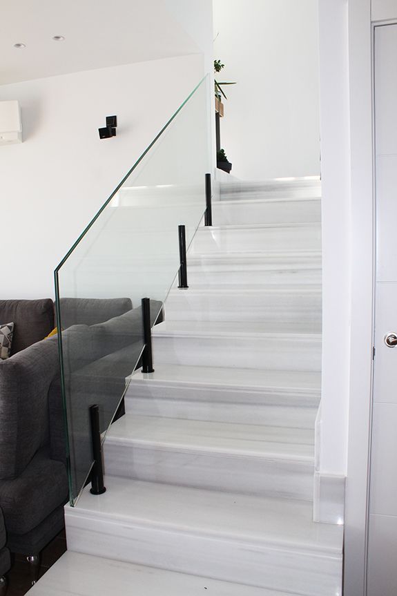 Una escalera blanca con barandilla de cristal en una sala de estar.