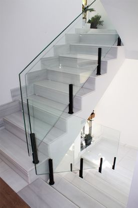 Una escalera con barandilla de cristal y escalones blancos.