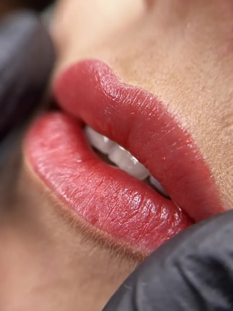 Primer plano de unos labios rosados ​​brillantes con un delineador de labios rojo oscuro y una mano