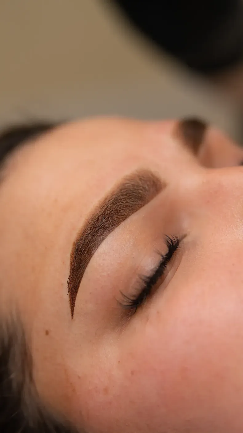 Primer plano de un ojo cerrado con una ceja oscura y bien definida y un maquillaje uniforme en la piel.