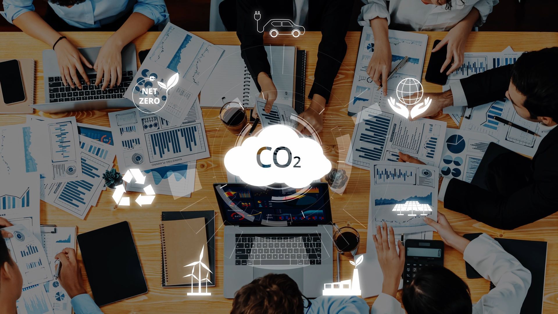 Vue en plongée de personnes travaillant autour d'un bureau avec des graphiques et des ordinateurs portables, sur lesquels se superposent des icônes représentant le CO2 et l'industrie.