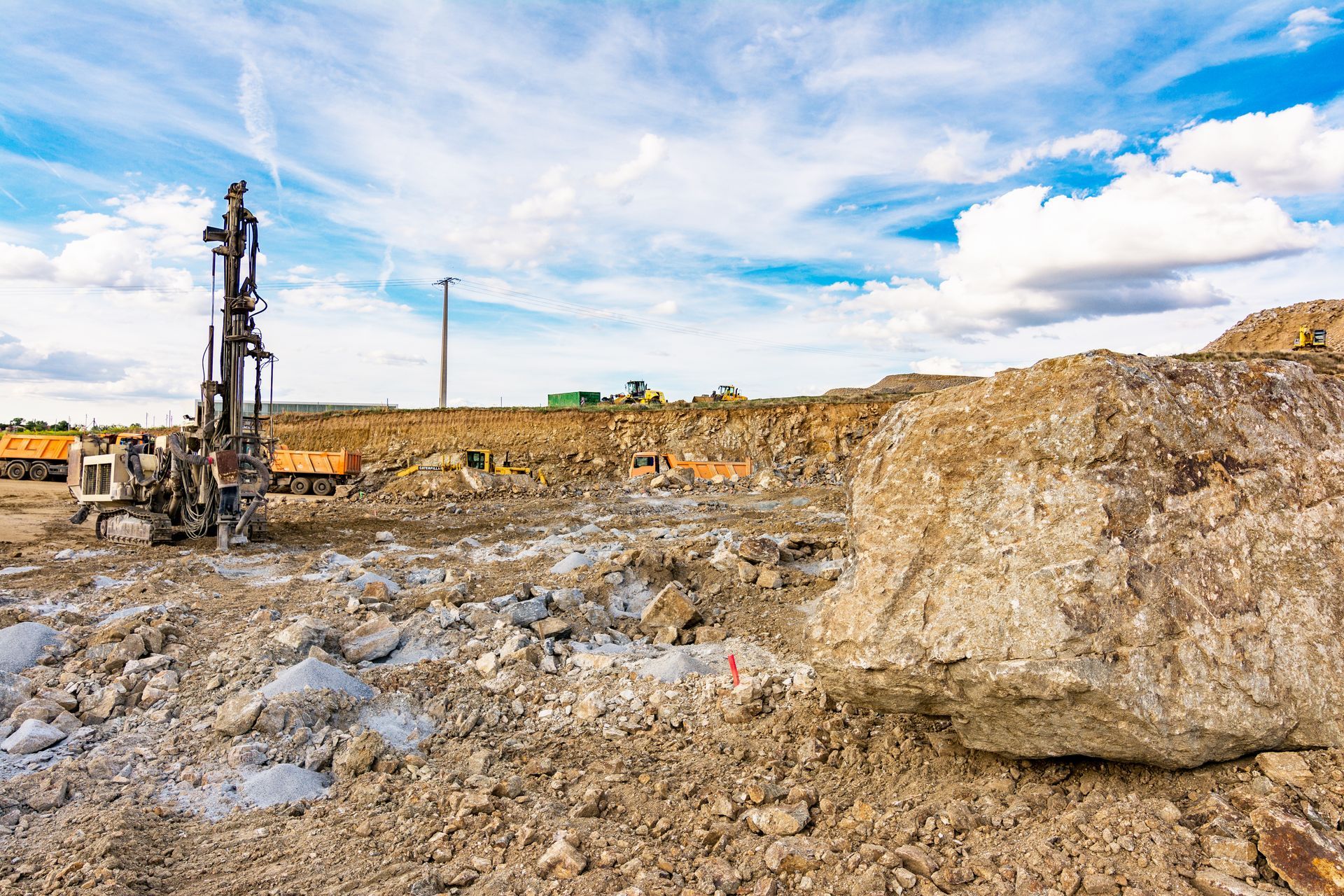 Installation de forage industriel dans une grande carrière rocheuse sous un ciel bleu parsemé de nuages.