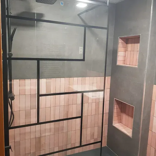 Un baño con azulejos rosas y una ducha a ras de suelo con marco negro.