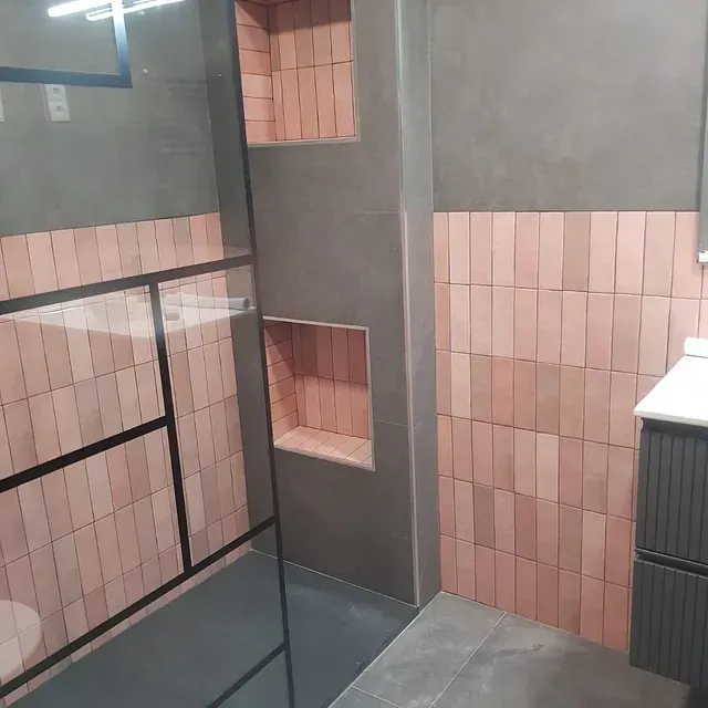 Un baño con azulejos rosas y ducha a ras de suelo.