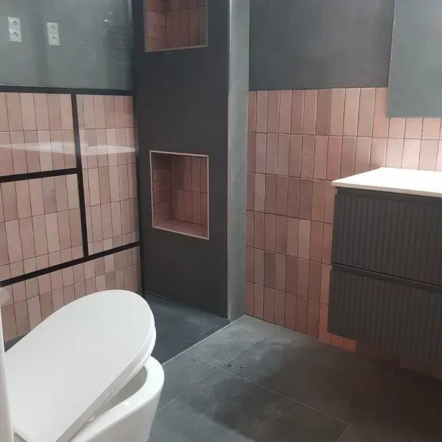 Un baño con inodoro, lavabo, espejo y azulejos rosas.