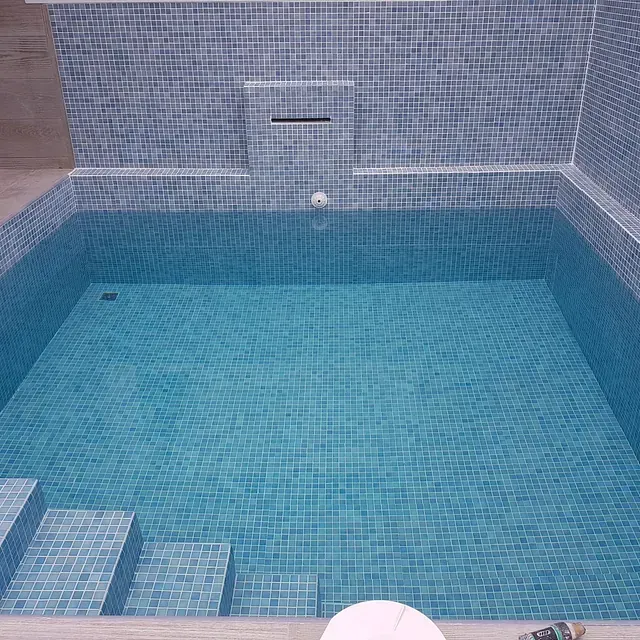 Una gran piscina con azulejos azules y una cascada.