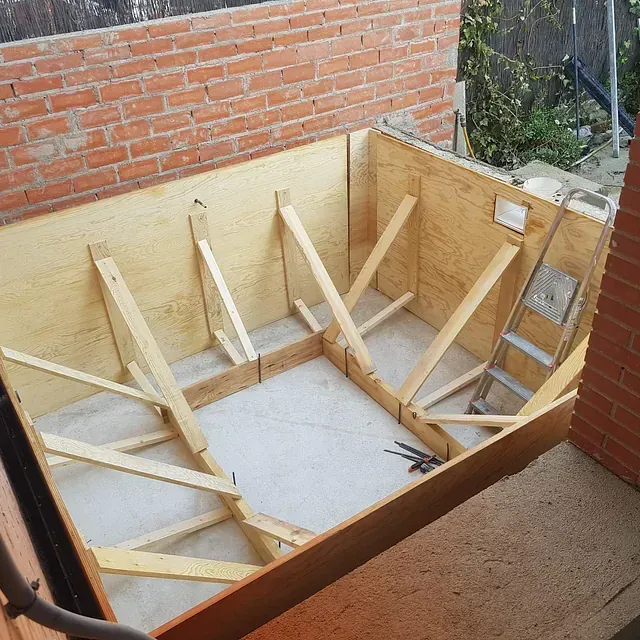 Una caja de madera con una escalera atada a ella frente a una pared de ladrillos.
