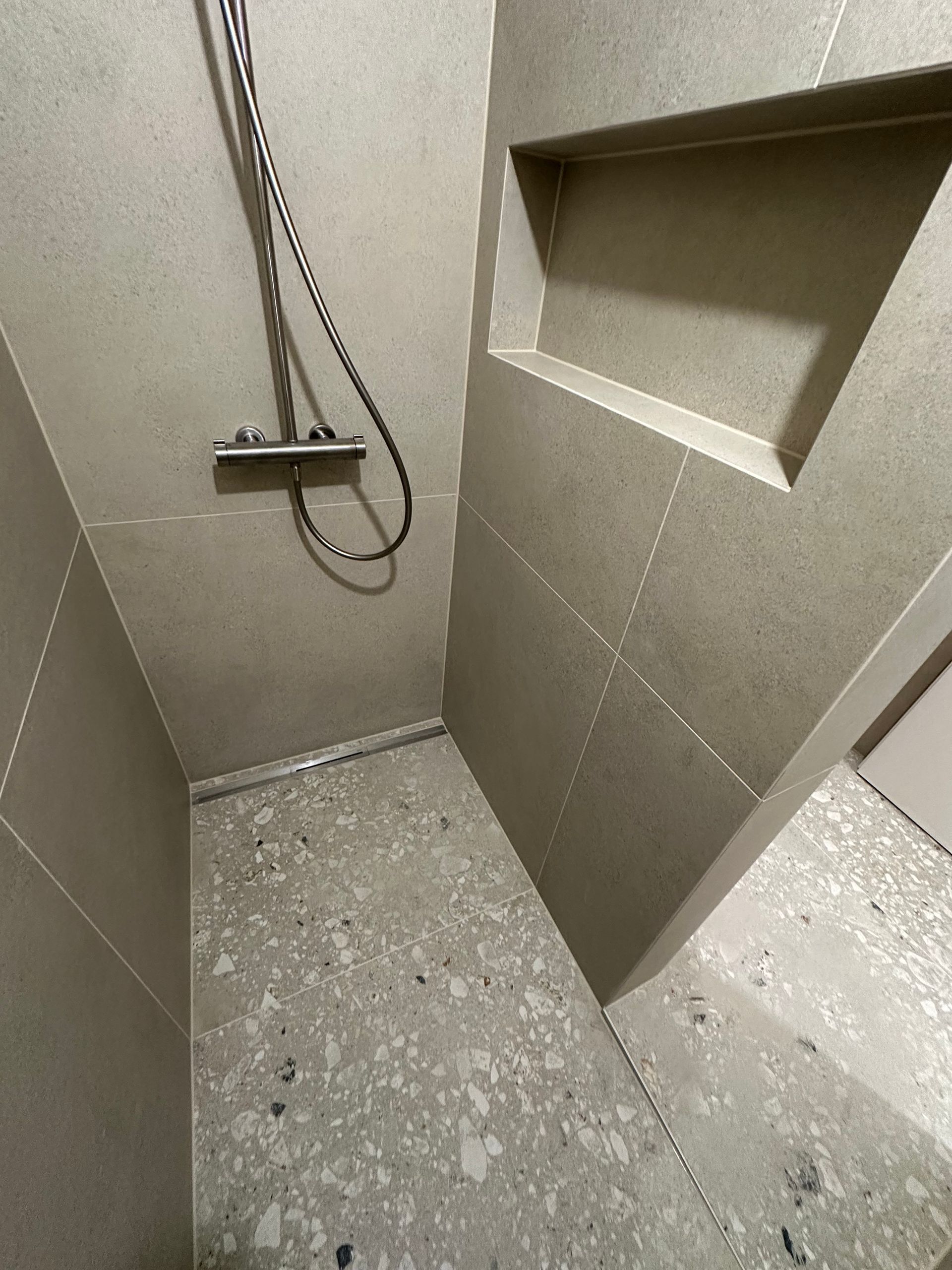 Douche carrelée de bleu avec étagère intégrée, pommeau de douche et mur recouvert de petits carreaux carrés.