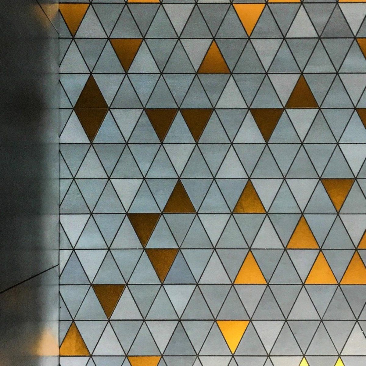 Mur à motifs triangulaires gris et or. Ombre à gauche.