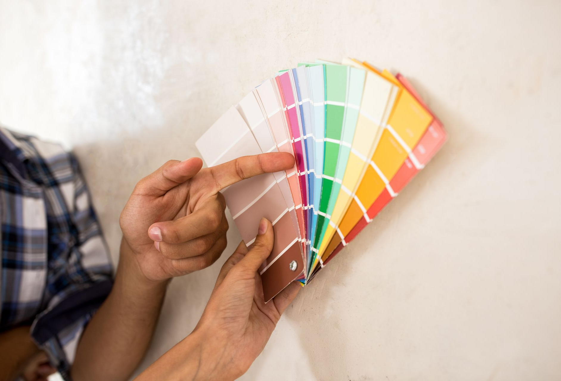 Une personne tenant une palette de couleurs compare des échantillons de peinture à un mur. Différentes couleurs vives sont présentées.