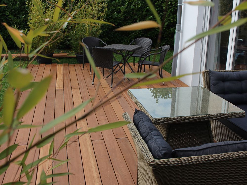 Holzterrasse mit Gartenmöbeln, darunter Stühle und Tisch, im Vordergrund Bambus.