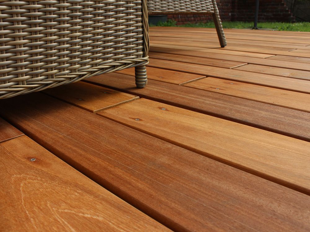 Holzterrasse mit einem Stuhlbein aus Korbgeflecht. Die Terrasse ist braun im natürlichen Licht.